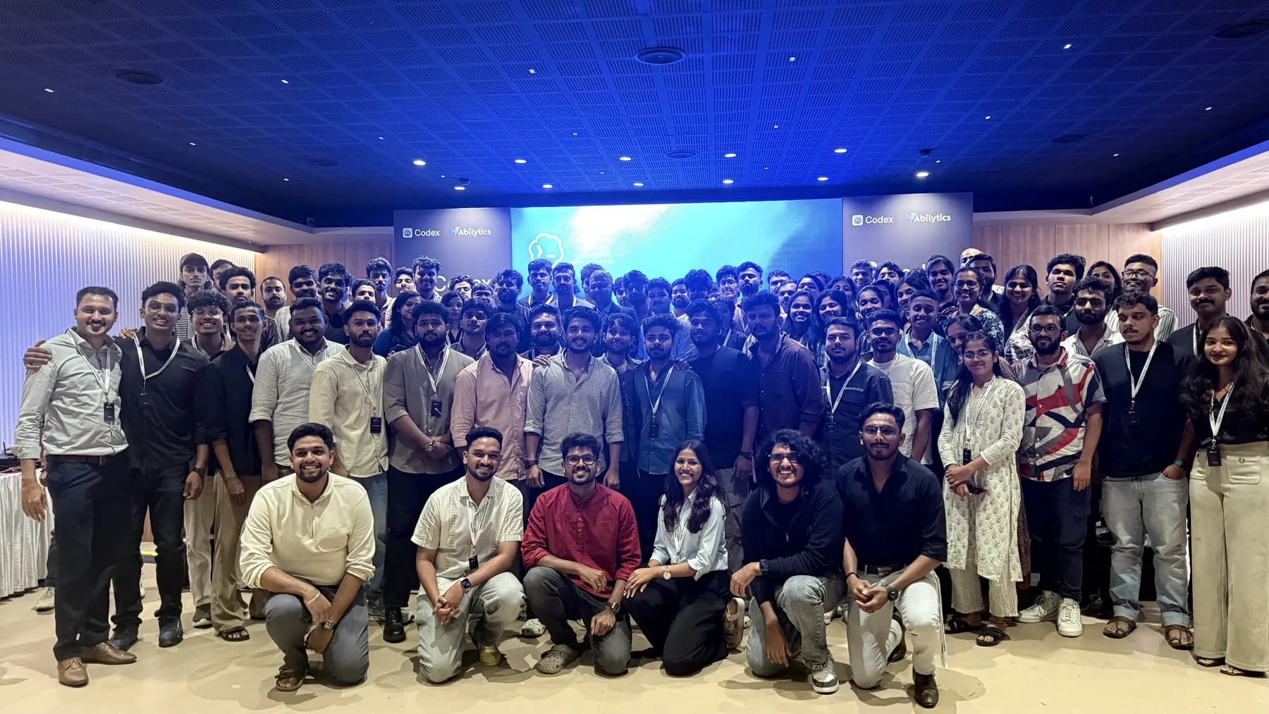 Large technology community group photo in a blue-lit hall