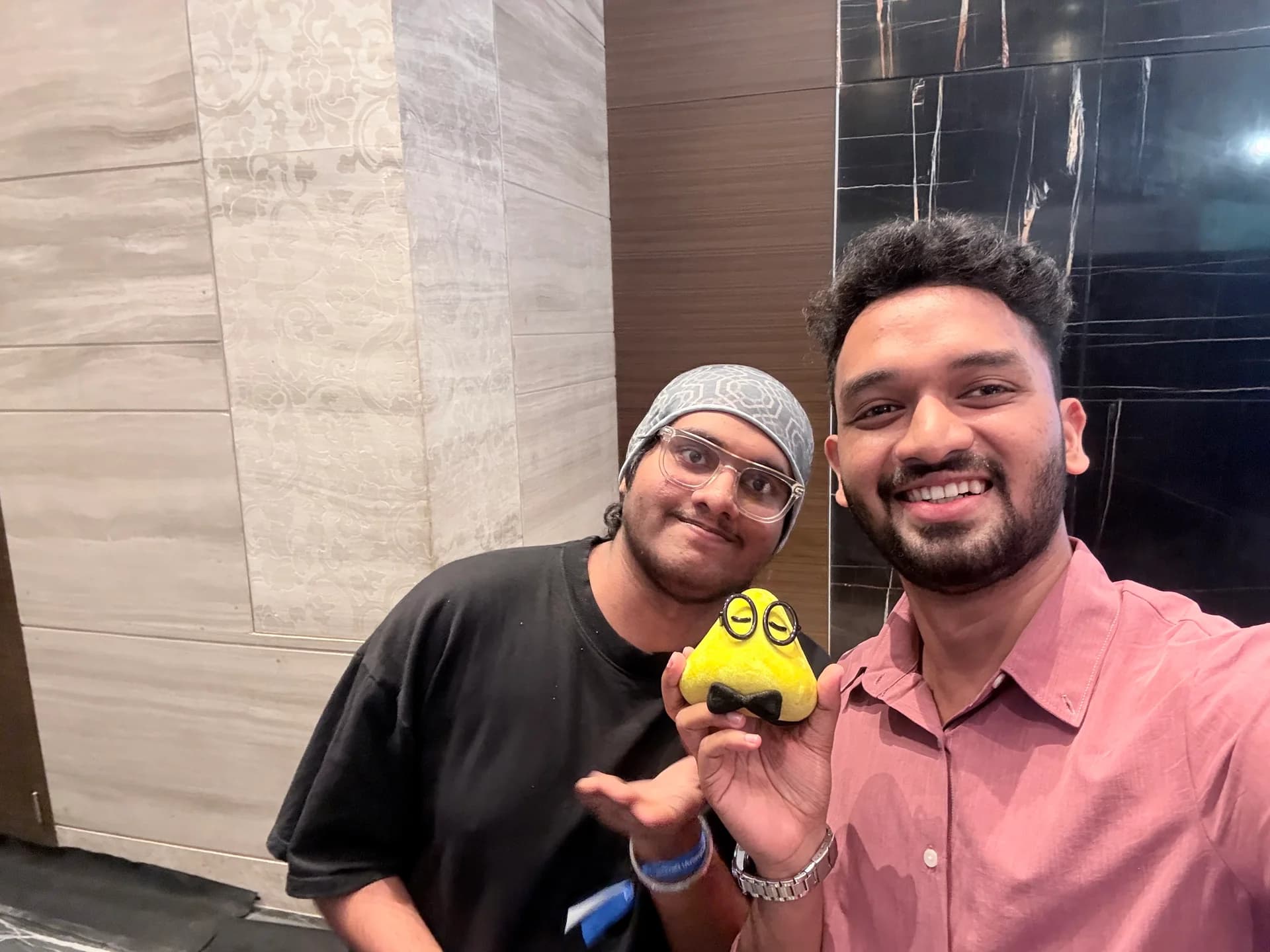 Robin Francis posing with a fellow DevDay attendee and the yellow builder mascot in Bengaluru